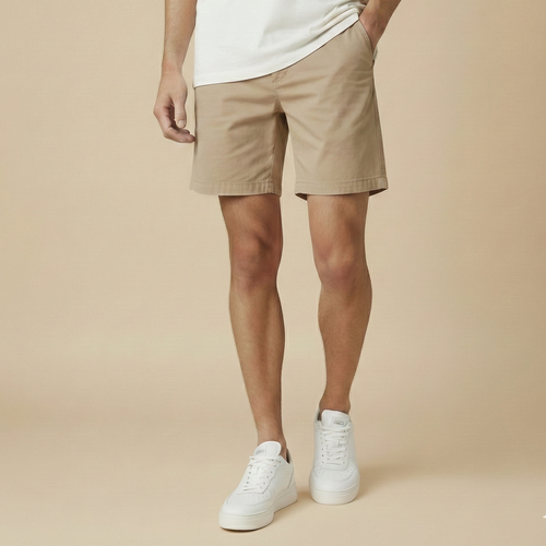 Person wearing beige shorts and white sneakers on a beige background